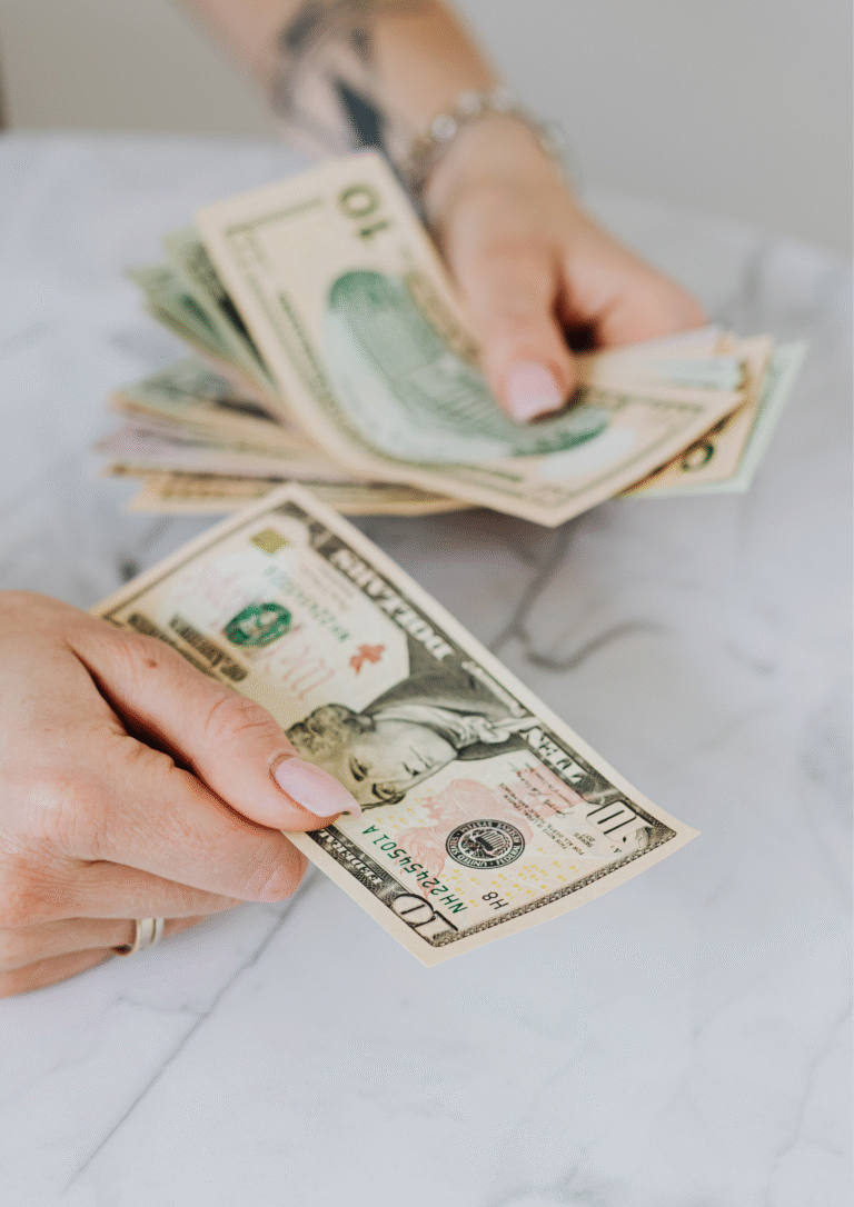 Hands holding and counting multiple U.S. dollar bills on a marble surface, symbolizing financial provision and blessing.