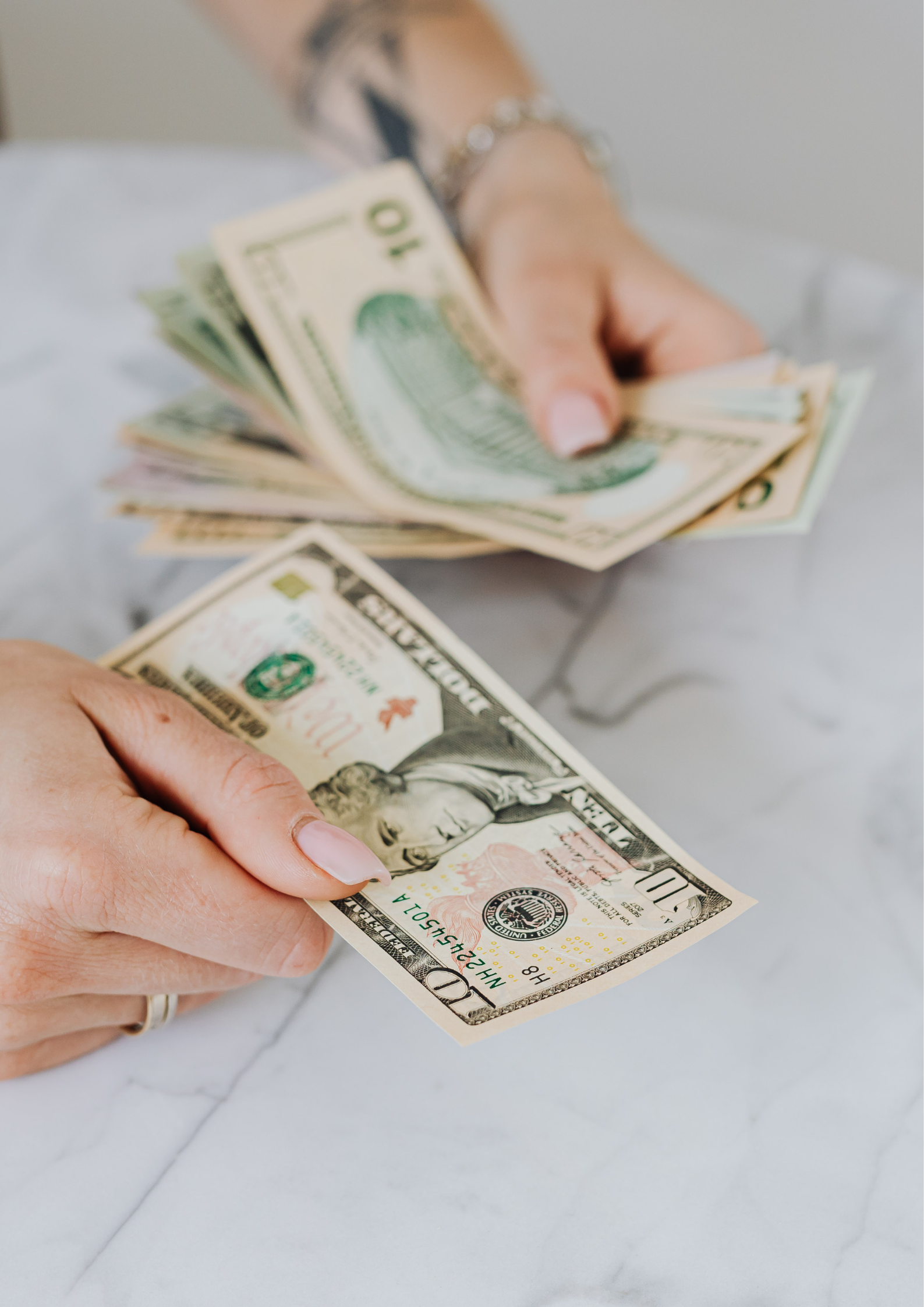 Hands holding and counting multiple U.S. dollar bills on a marble surface, symbolizing financial provision and blessing.