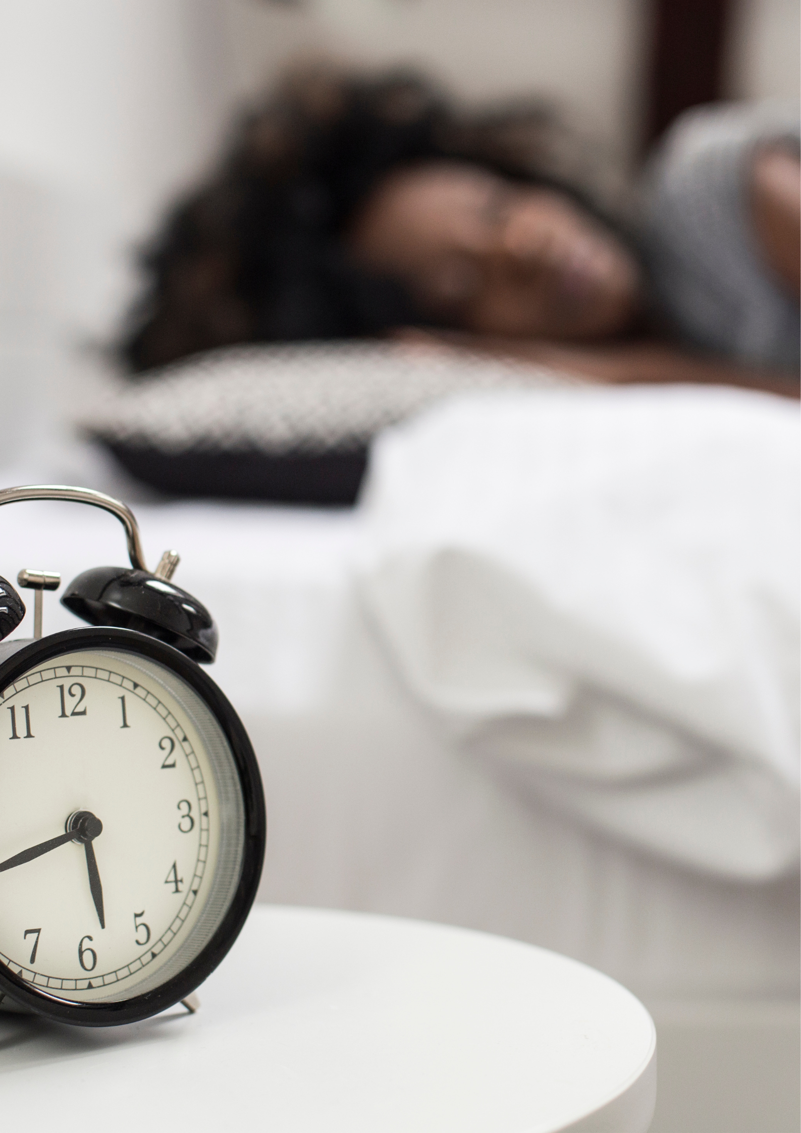 Black alarm clock on a bedside table with a person sleeping in the background, symbolizing peaceful rest at night.
